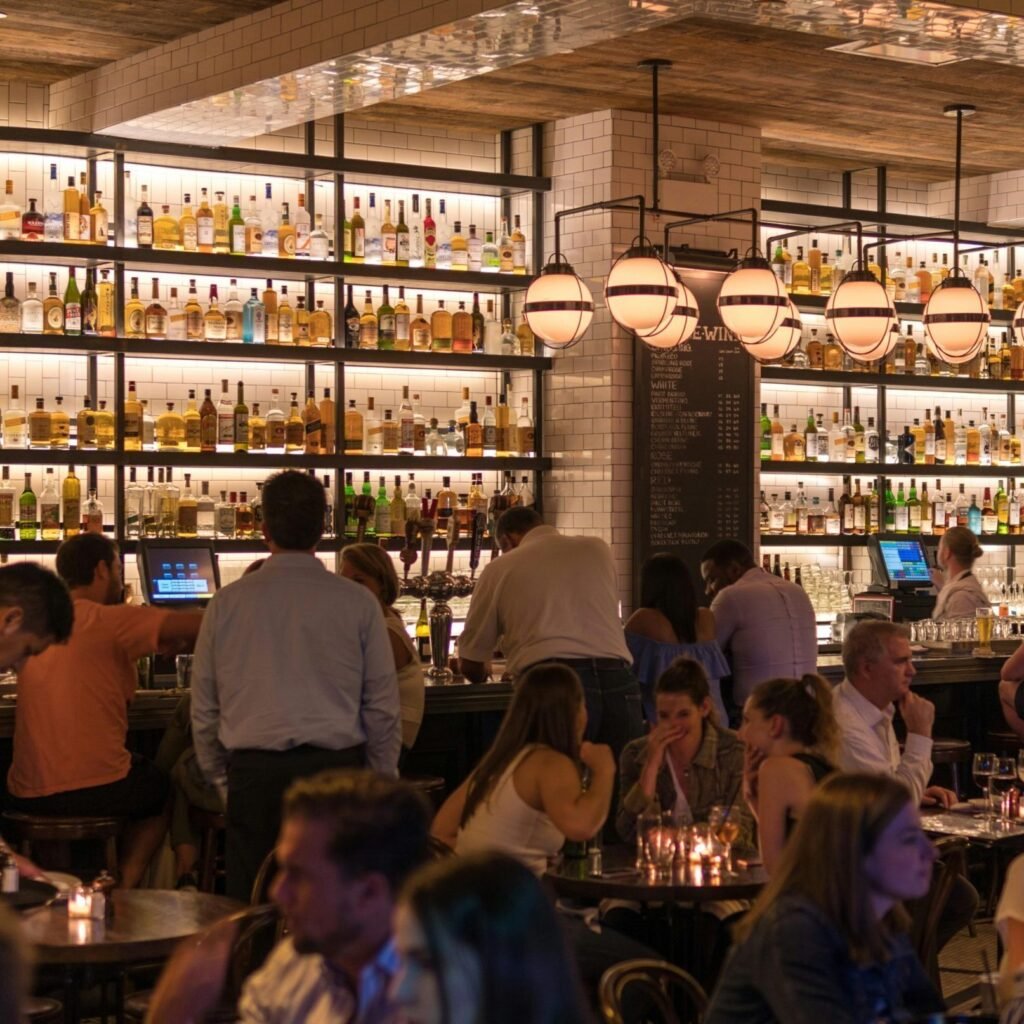Experience the lively atmosphere of a bustling New York City bar with patrons enjoying nightlife within a stylish indoor setting.